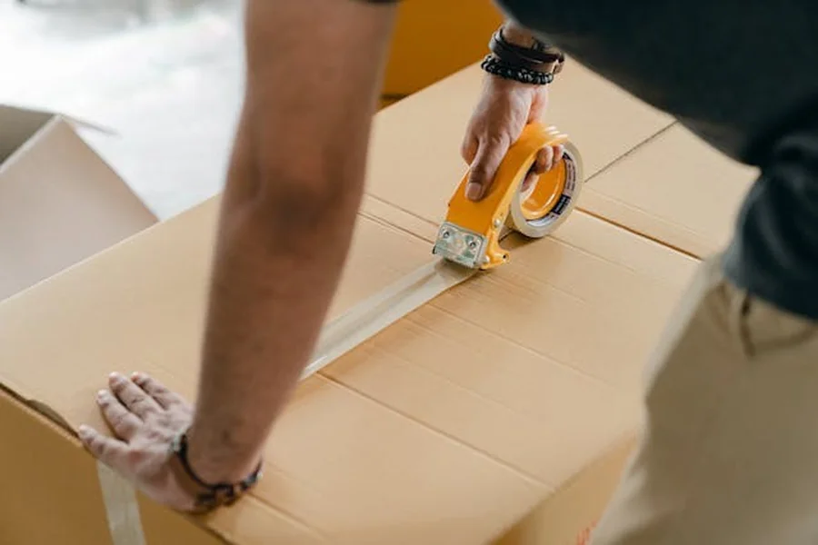 A man sealing a cardboard box with a tape