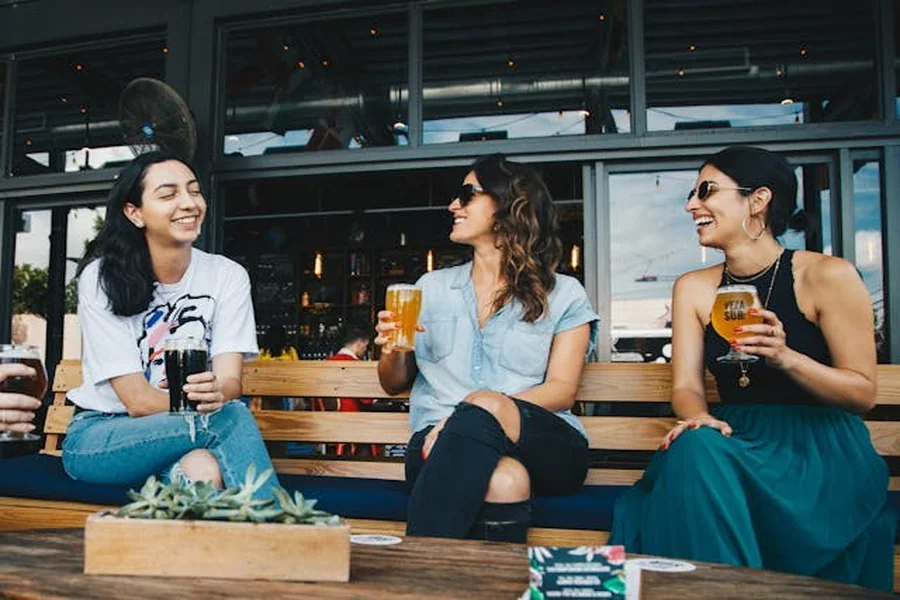Three friends sitting on a bench, talking and drinking